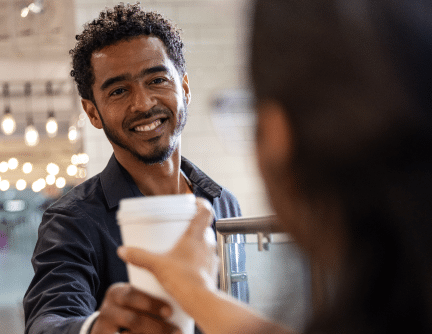 Male barista smiling and handing a customer a white cup of coffee