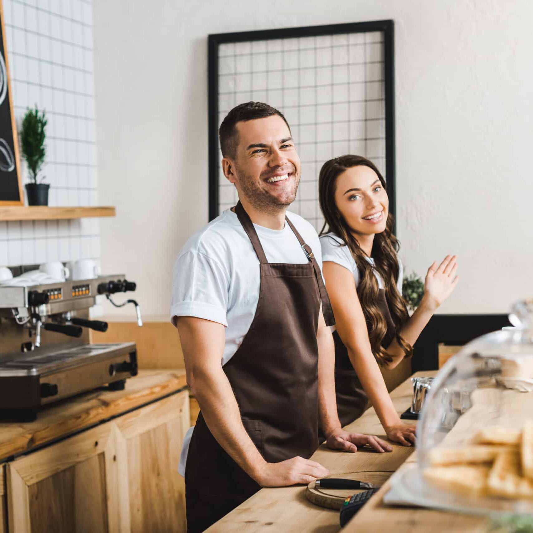 Two baristas smiling behind counter, coffee and tea café, espresso machine on counter