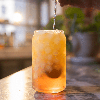 Iced tea in a glass being stirred by a metal spoon
